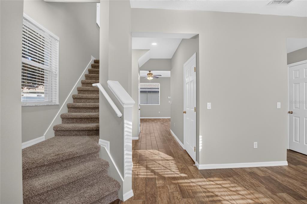 A carpeted staircase leads upstairs next to a hallway with wood-look flooring and white doors — 8832 DANFORTH DRIVE, WINDERMERE, FL