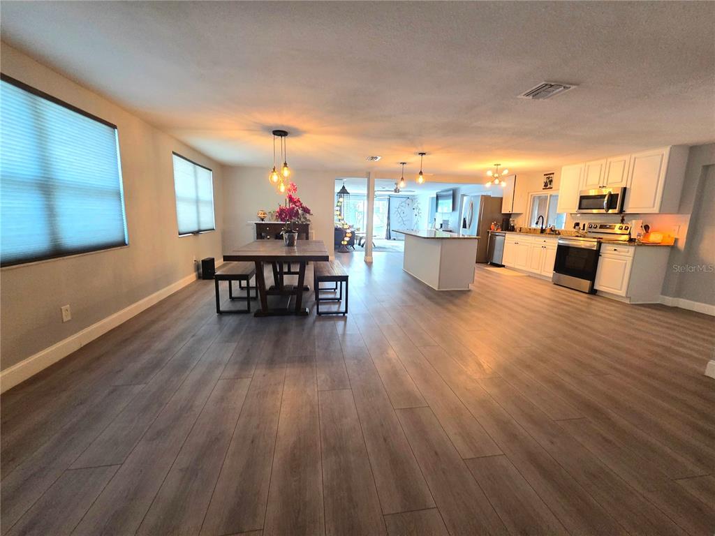 An open-concept kitchen and dining area with light wood-look flooring and white cabinetry — 9820 POCONO STREET, PORT RICHEY, FL