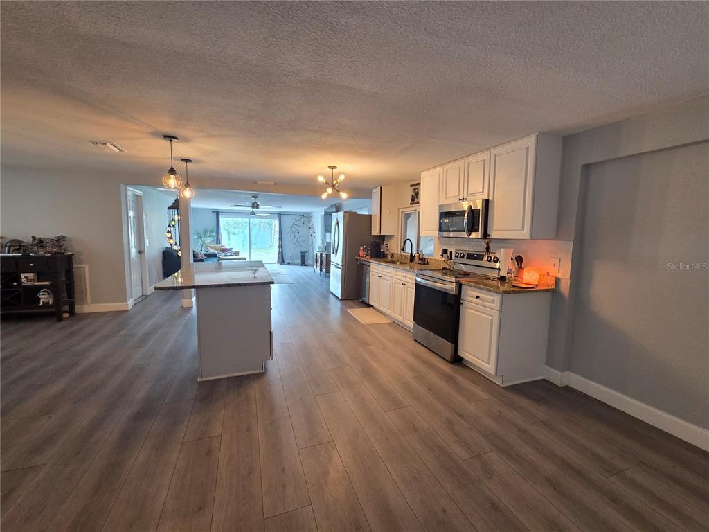A kitchen with white cabinets, stainless steel appliances, and a central island with wood flooring — 9820 POCONO STREET, PORT RICHEY, FL