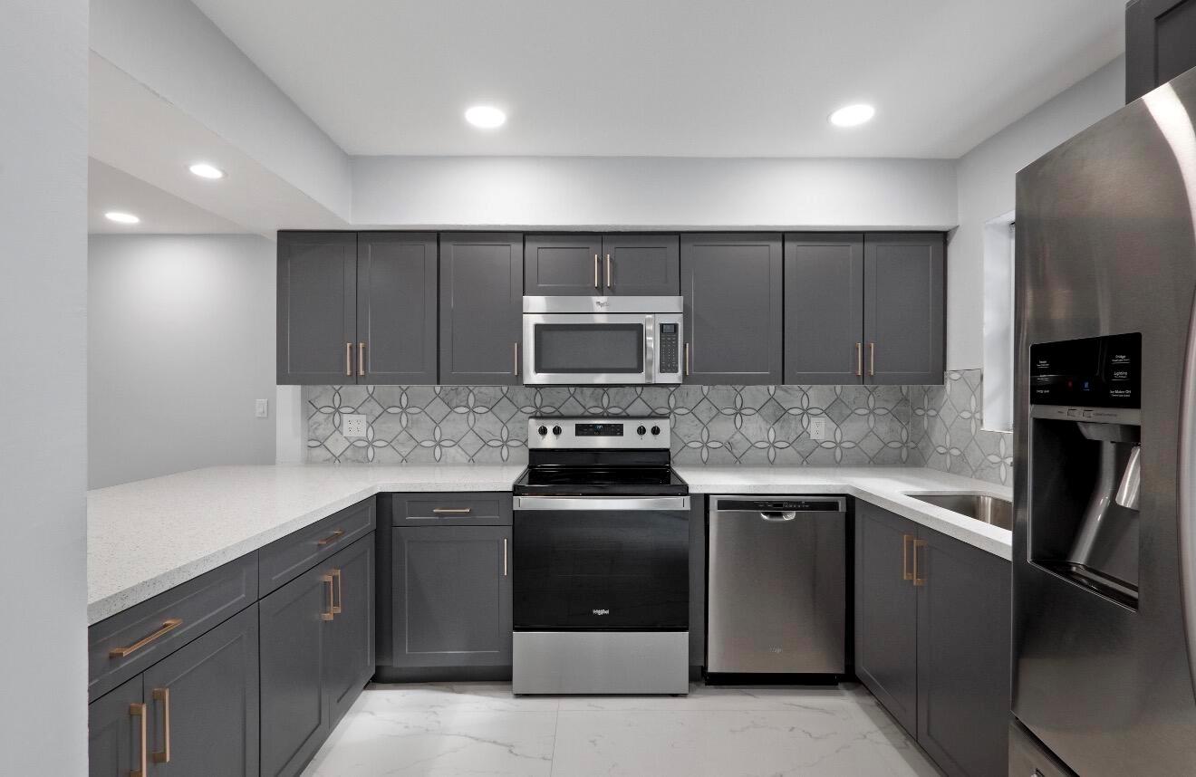 A modern kitchen features dark gray cabinets, stainless steel appliances, and a patterned tile backsplash — 1661 NW 1st Avenue, Pompano Beach FL 33060, POMPANO BEACH, FL