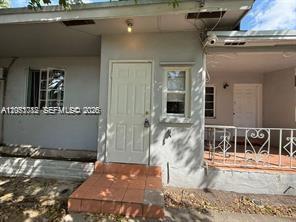 A single-story house exterior features a white front door, a window, and a covered porch — MIAMI, FL