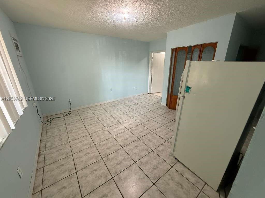 A kitchen with light blue walls, white tile flooring, and a white refrigerator — MIAMI, FL