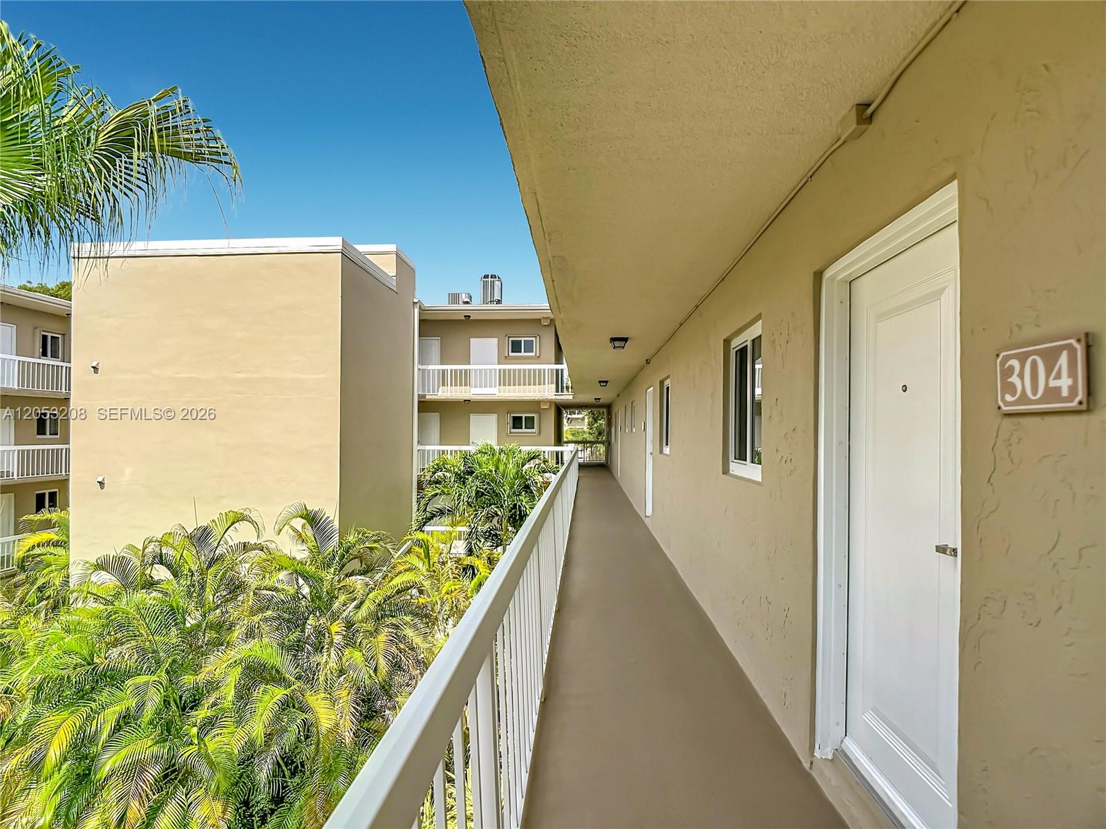 An outdoor walkway leads past apartment unit 304 with palm trees visible below — 7722 Camino Real # E304, Miami FL 33143, MIAMI, FL