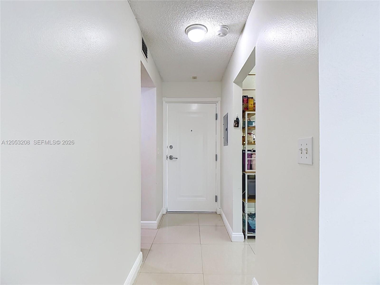 A white hallway features tile flooring, a central ceiling light, and a white entry door — 7722 Camino Real # E304, Miami FL 33143, MIAMI, FL