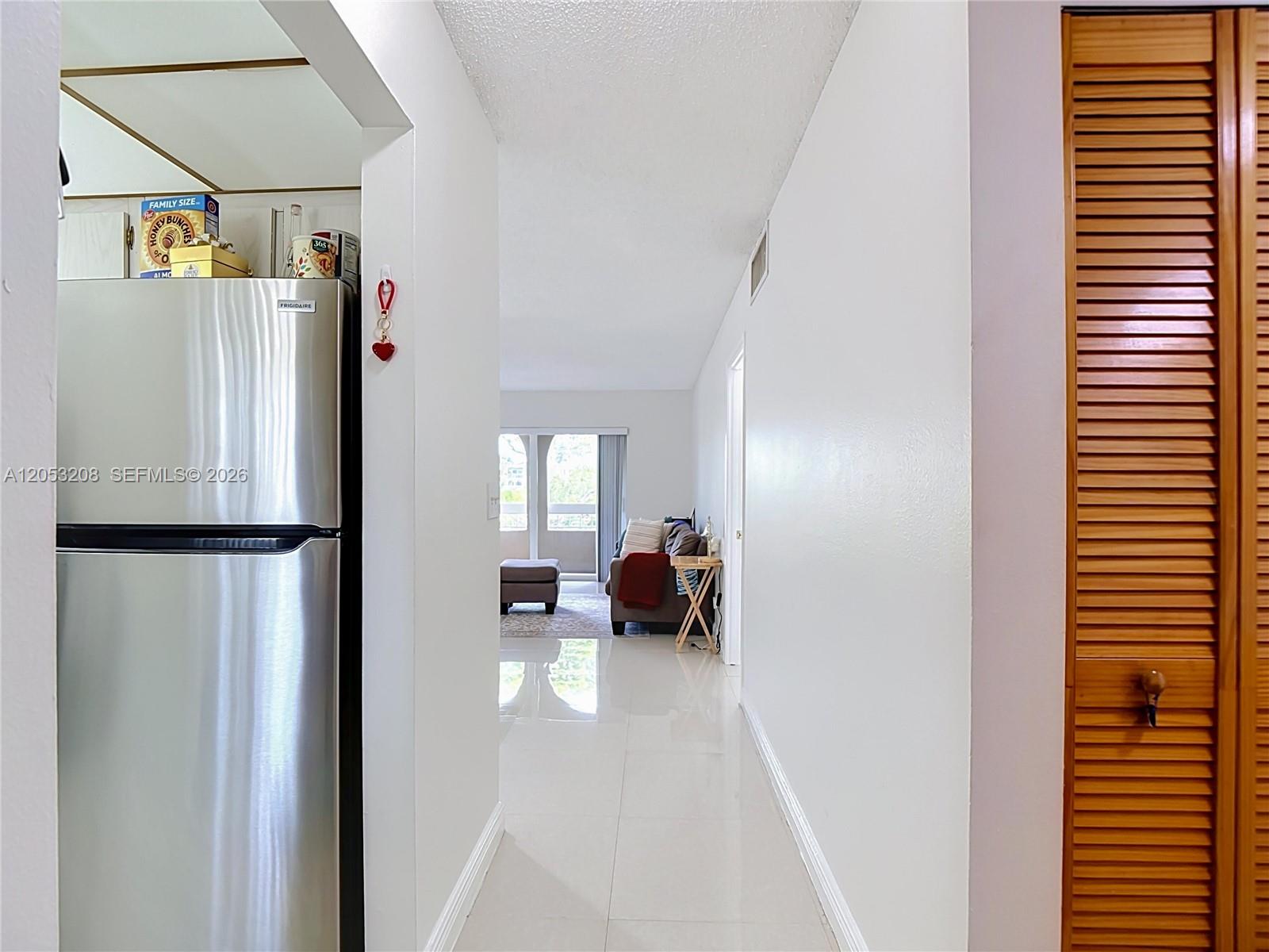 A hallway with white tile floors leads from a kitchen area toward a living room — 7722 Camino Real # E304, Miami FL 33143, MIAMI, FL
