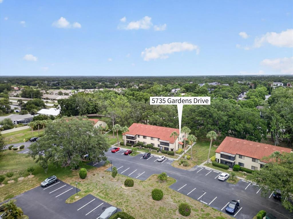 An aerial view shows two multi-story apartment buildings with red tile roofs and parking lots — 5735 GARDENS DRIVE UNIT 5735, SARASOTA, FL