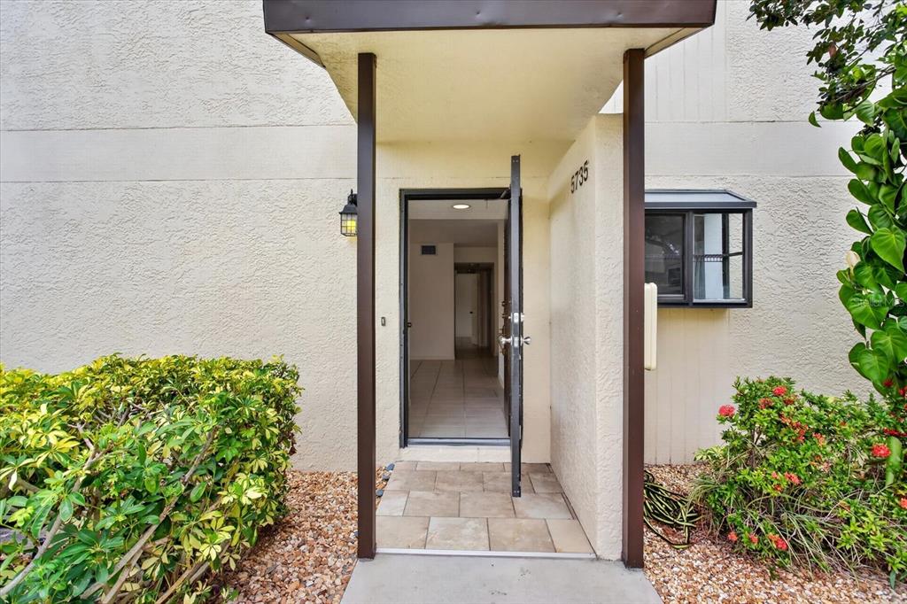 The exterior entrance features a covered walkway, a tiled porch, and a partially open door — 5735 GARDENS DRIVE UNIT 5735, SARASOTA, FL