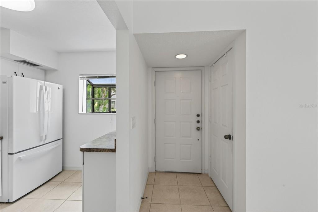 A white kitchen with a refrigerator and a tiled entryway featuring a front door — 5735 GARDENS DRIVE UNIT 5735, SARASOTA, FL