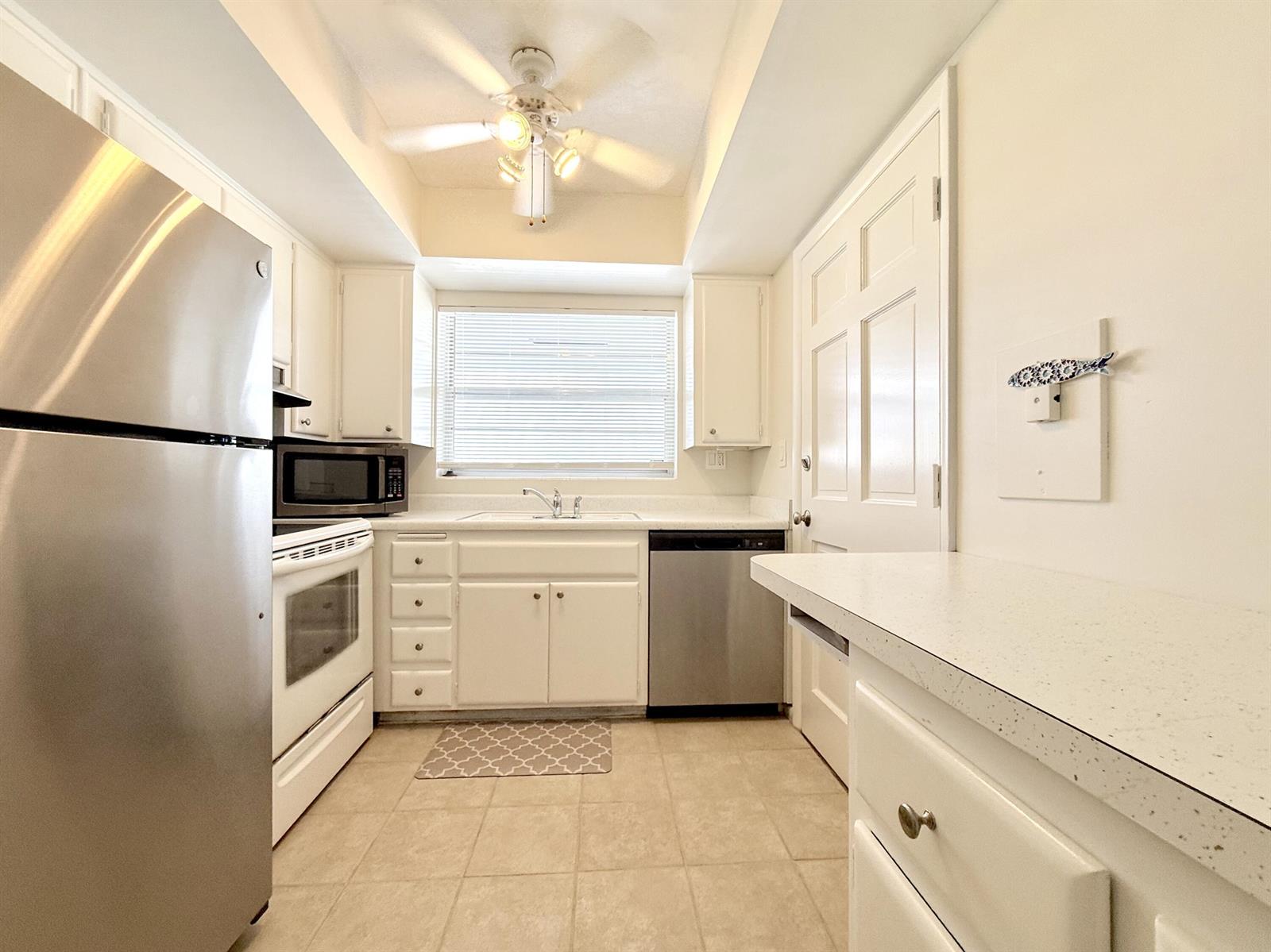 A kitchen features white cabinetry, stainless steel appliances, a ceiling fan, and tiled flooring — 50 Celestial Way # 305, Juno Beach FL 33408, JUNO BEACH, FL