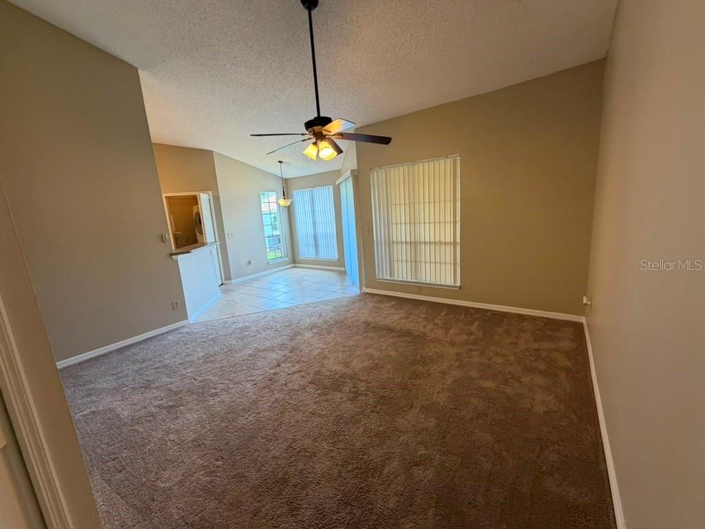 A living room with beige carpet, vaulted ceilings, a ceiling fan, and an adjacent dining area — 4807 NORMANDY PLACE UNIT 202, ORLANDO, FL