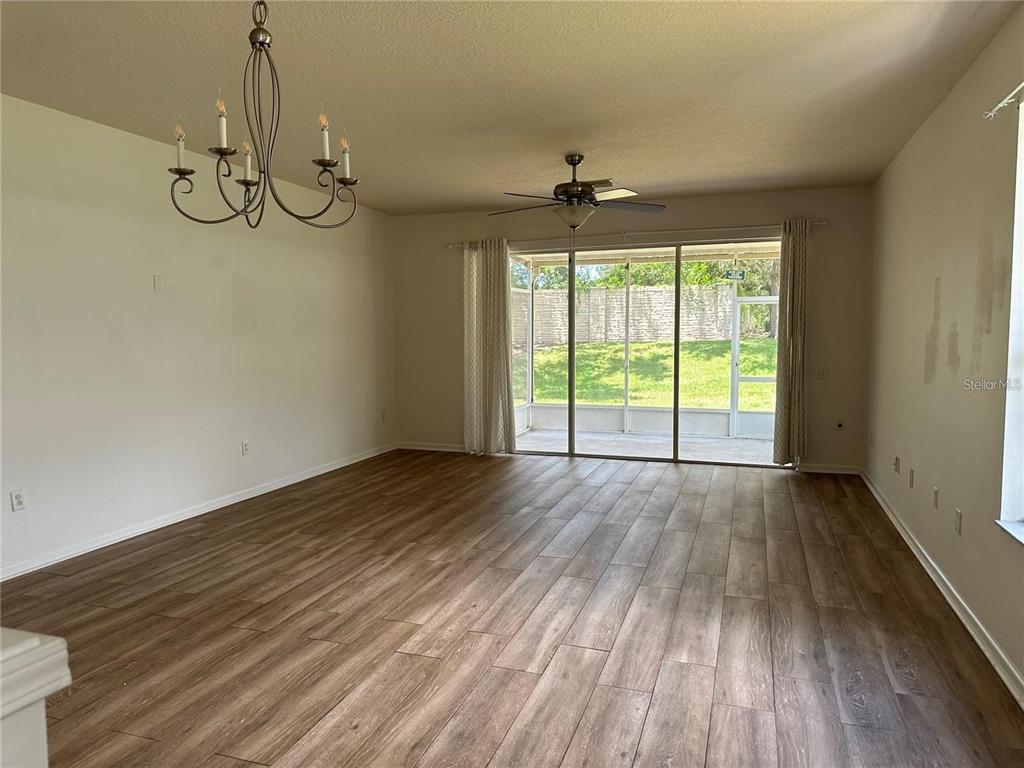 A spacious living room with wood-look flooring, a chandelier, a ceiling fan, and sliding doors — 7163 83RD DRIVE E, BRADENTON, FL