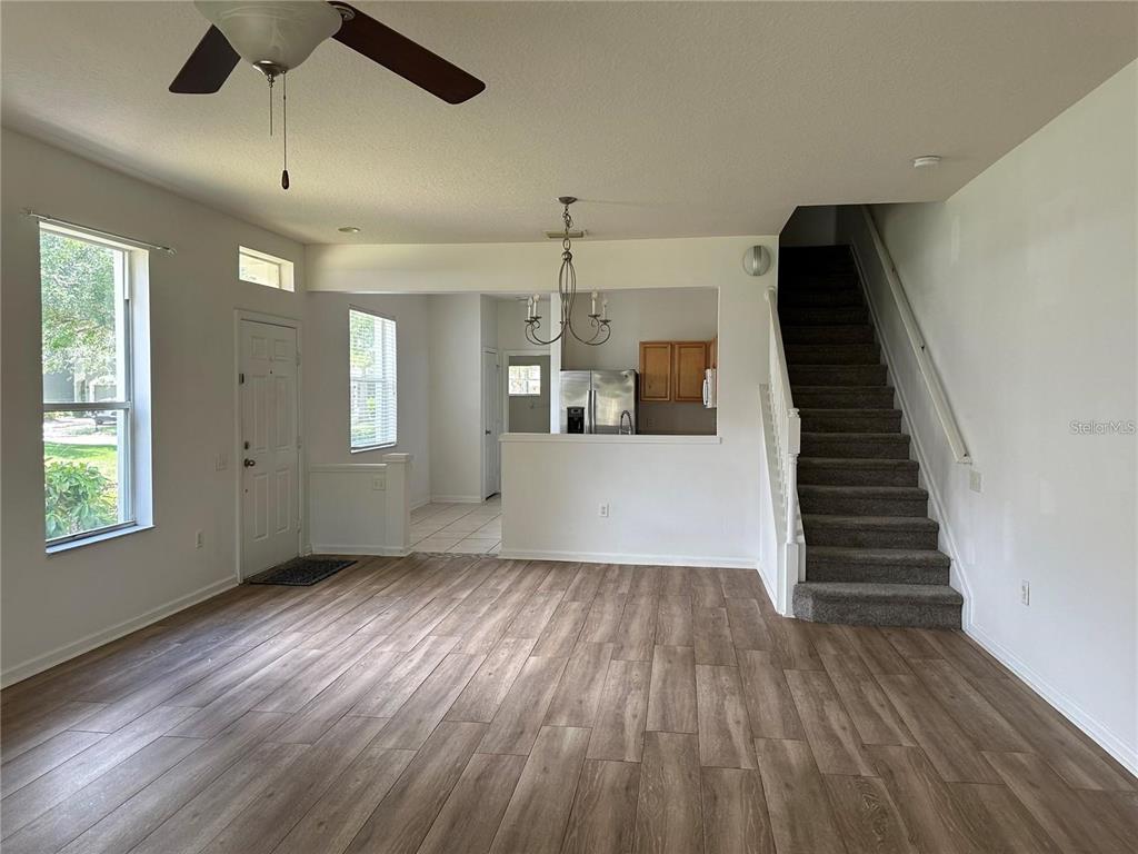 A living room with wood-look flooring, a staircase, and an open view into the kitchen — 7163 83RD DRIVE E, BRADENTON, FL