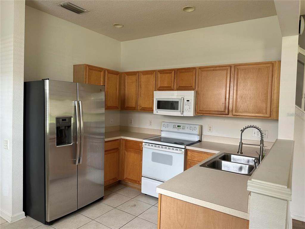 A kitchen features light wood cabinets, white appliances, a stainless steel refrigerator, and tiled floors — 7163 83RD DRIVE E, BRADENTON, FL