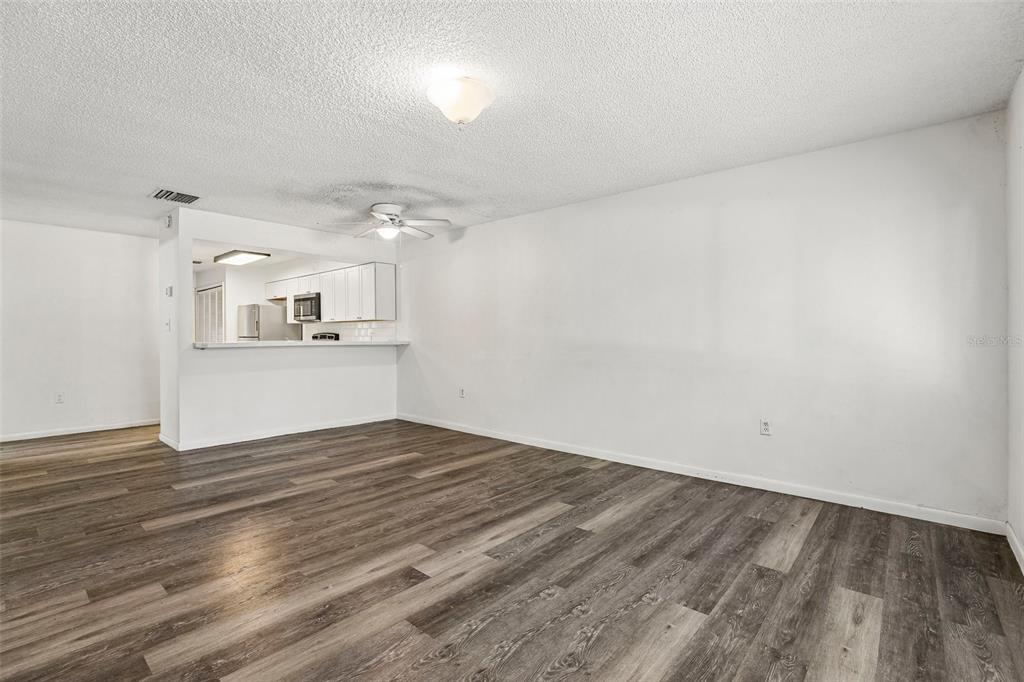 An empty living room with wood-look flooring, a ceiling fan, and an open kitchen pass-through — 904 SUMTER STREET, LEESBURG, FL