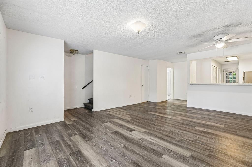 An empty living room features wood-look flooring, white walls, a ceiling fan, and a staircase — 904 SUMTER STREET, LEESBURG, FL