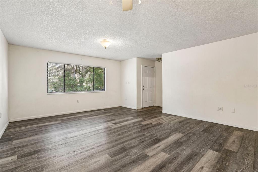 An empty living room features gray wood-look flooring, white walls, and a large window — 904 SUMTER STREET, LEESBURG, FL