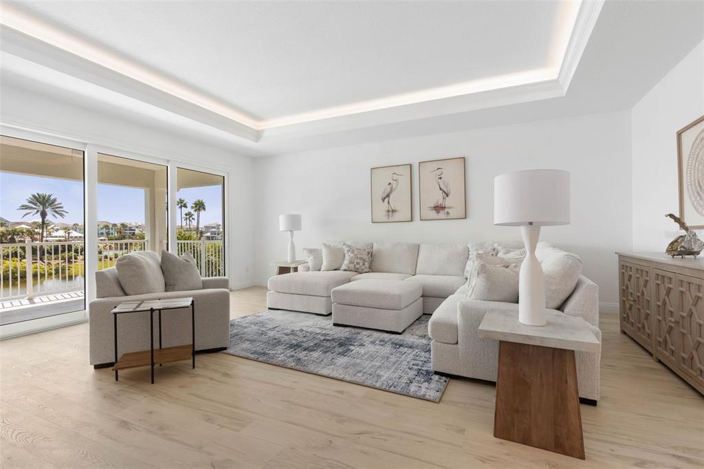 A bright living room features a sectional sofa, light wood floors, and a balcony view — 18 CINNAMON BEACH WAY, PALM COAST, FL