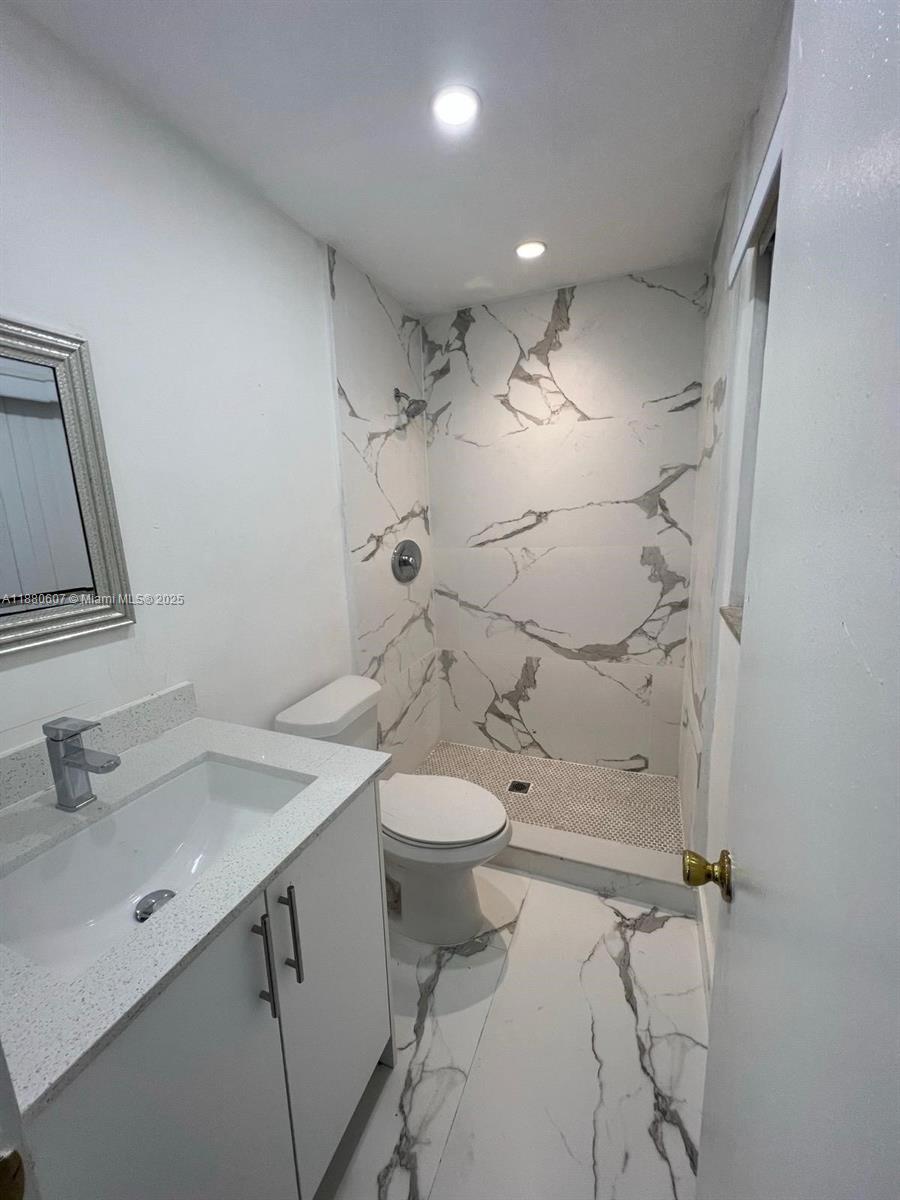 A bathroom features a white vanity, a toilet, and a walk-in shower with marble-patterned tiles — 222 SW 8th St # C, Dania Beach FL 33004, DANIA BEACH, FL