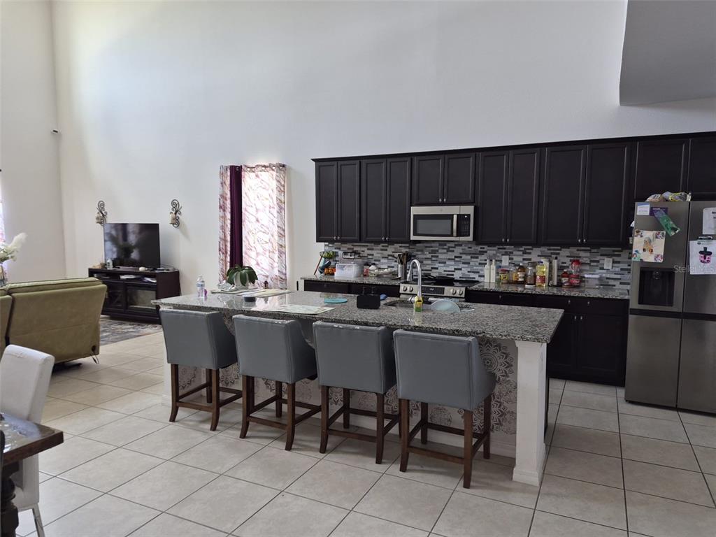 A kitchen features dark cabinets, granite countertops, a central island with four chairs, and tile flooring — 1482 FLATWOOD STREET, ST CLOUD, FL