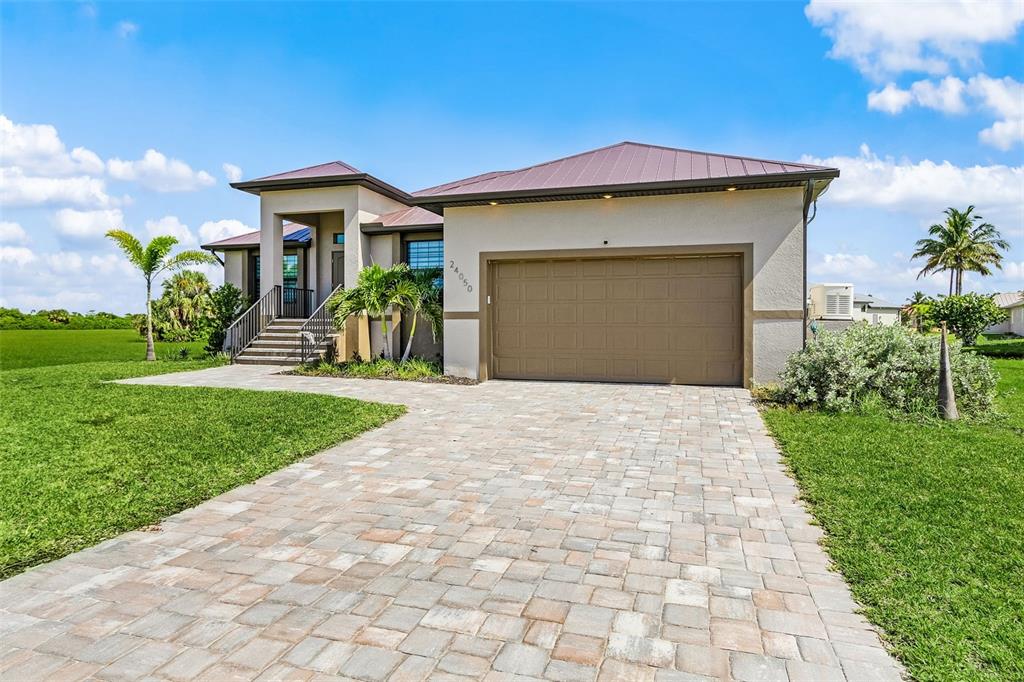 A single-story house with a metal roof, beige stucco exterior, and a paved driveway — 24050 BUNDY COURT, PUNTA GORDA, FL