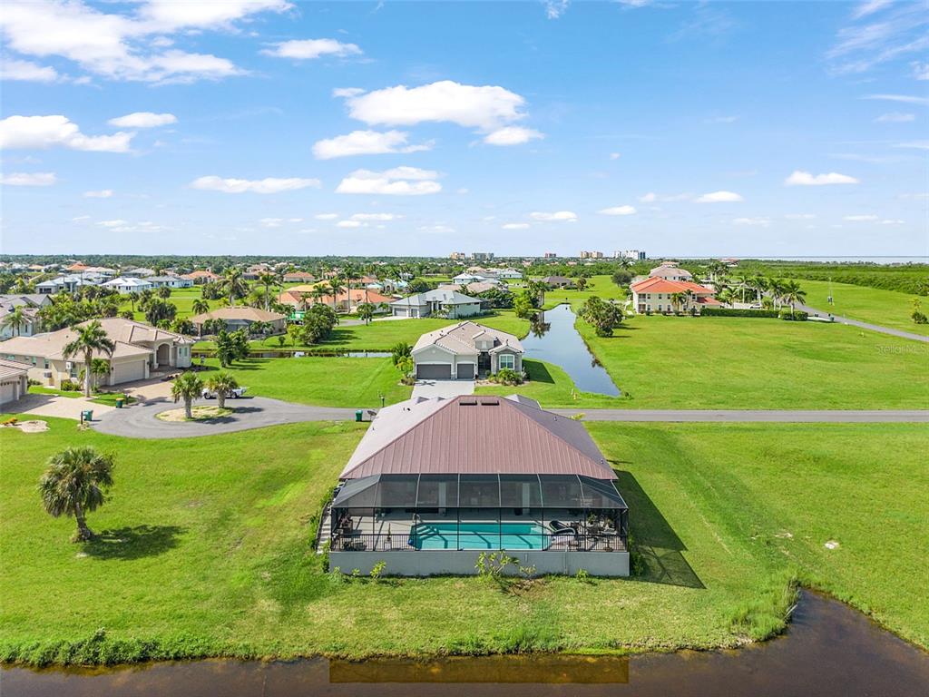 An aerial view shows a house with a screened-in pool overlooking a canal and fields — 24050 BUNDY COURT, PUNTA GORDA, FL