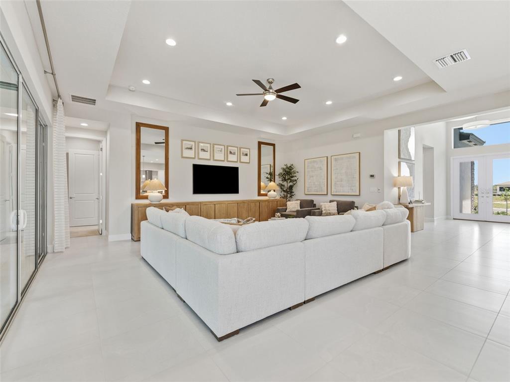 A spacious living room features a large white sectional sofa, a media console, and recessed lighting — 3857 CABERNET TERRACE, WESLEY CHAPEL, FL