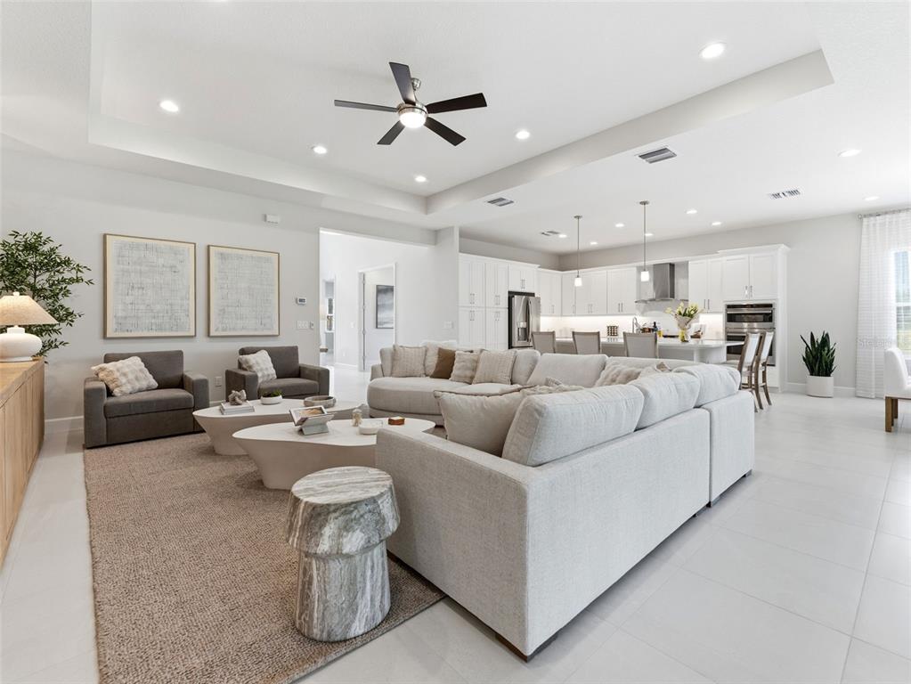 A spacious open-concept living room features a large sectional sofa, neutral decor, and white cabinetry — 3857 CABERNET TERRACE, WESLEY CHAPEL, FL