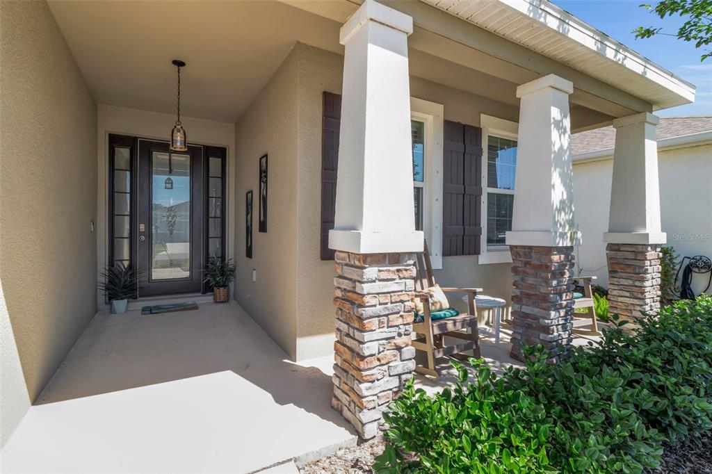 A covered front porch features stone-based columns, a glass-paneled front door, and a rocking chair — 13225 WATERLEAF GARDEN CIRCLE, RIVERVIEW, FL