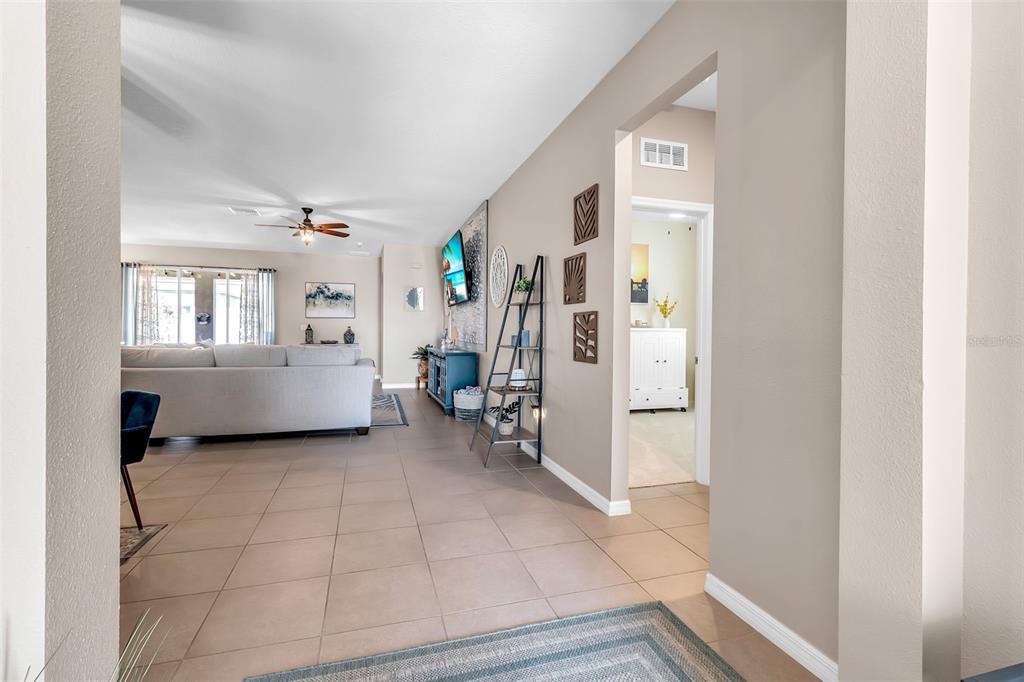 A view from a hallway looking into a living room with tile floors and furniture — 13225 WATERLEAF GARDEN CIRCLE, RIVERVIEW, FL
