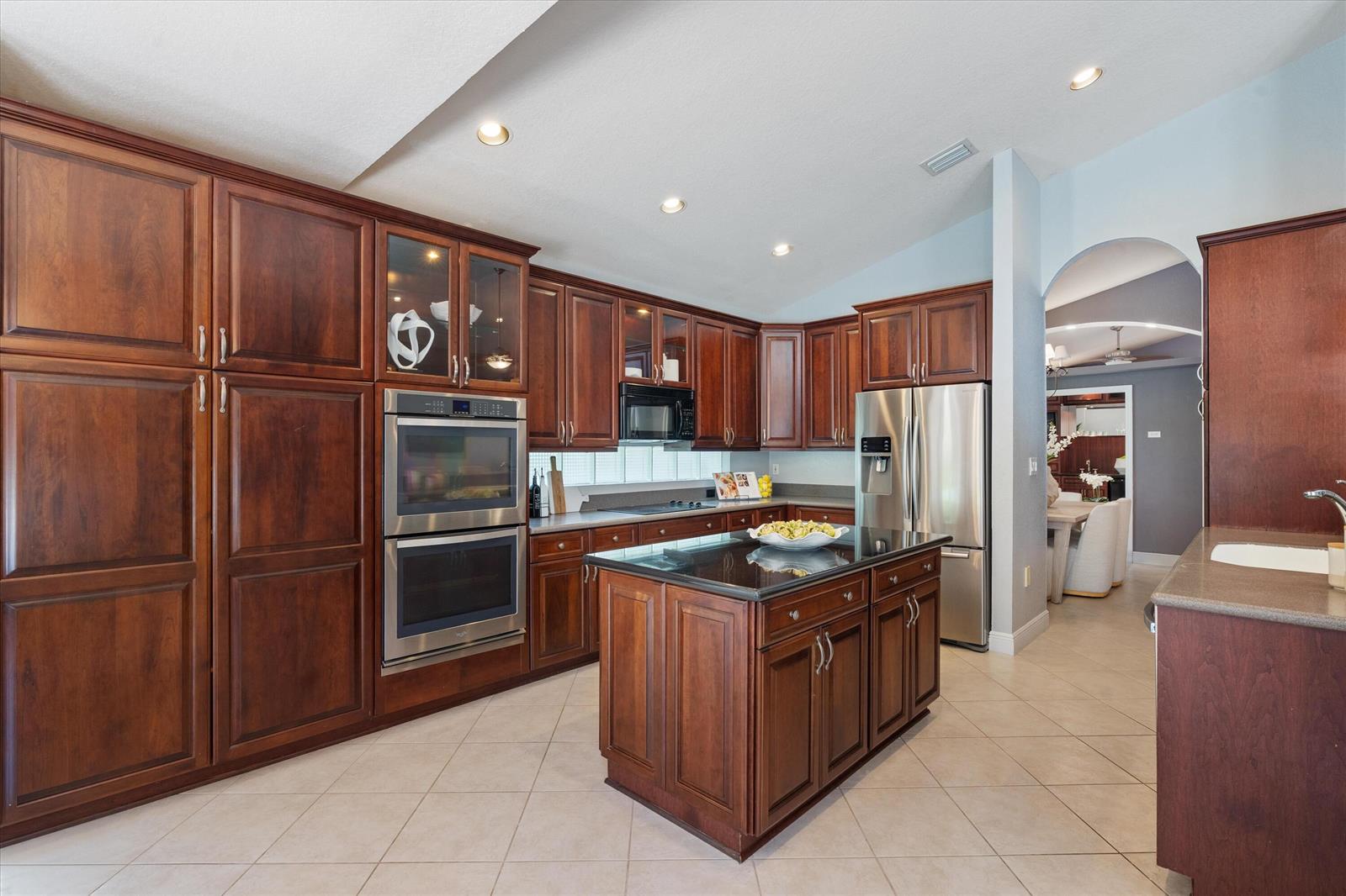 A kitchen features dark wood cabinetry, stainless steel appliances, a black island, and tile flooring — 19633 Estuary Drive, Boca Raton FL 33498, BOCA RATON, FL