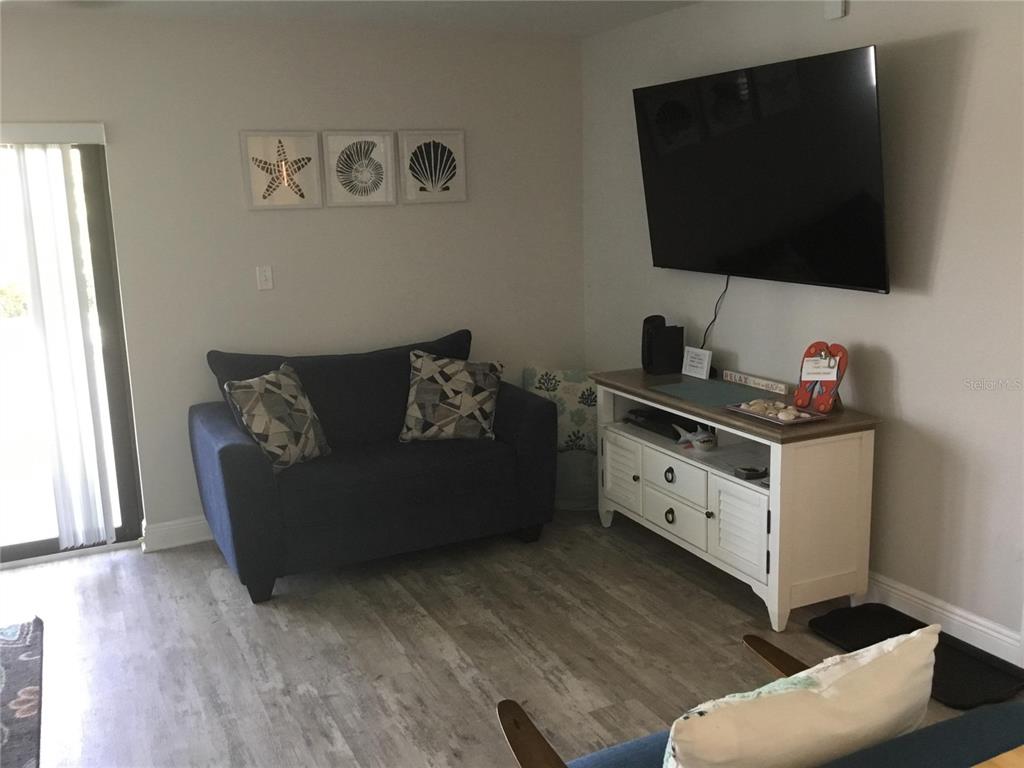 A living room features a blue loveseat, a white media console, and a wall-mounted television — 1571 S ATLANTIC AVENUE UNIT 212, NEW SMYRNA BEACH, FL
