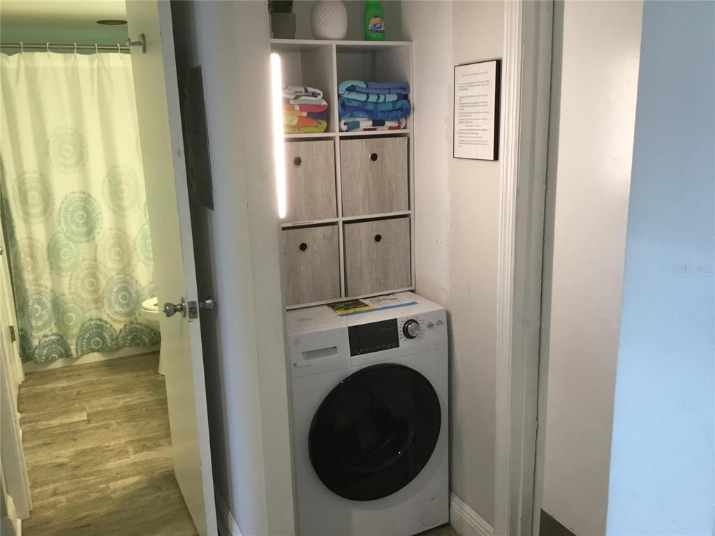 A laundry closet with a front-loading washer and open shelving sits beside a bathroom — 1571 S ATLANTIC AVENUE UNIT 212, NEW SMYRNA BEACH, FL