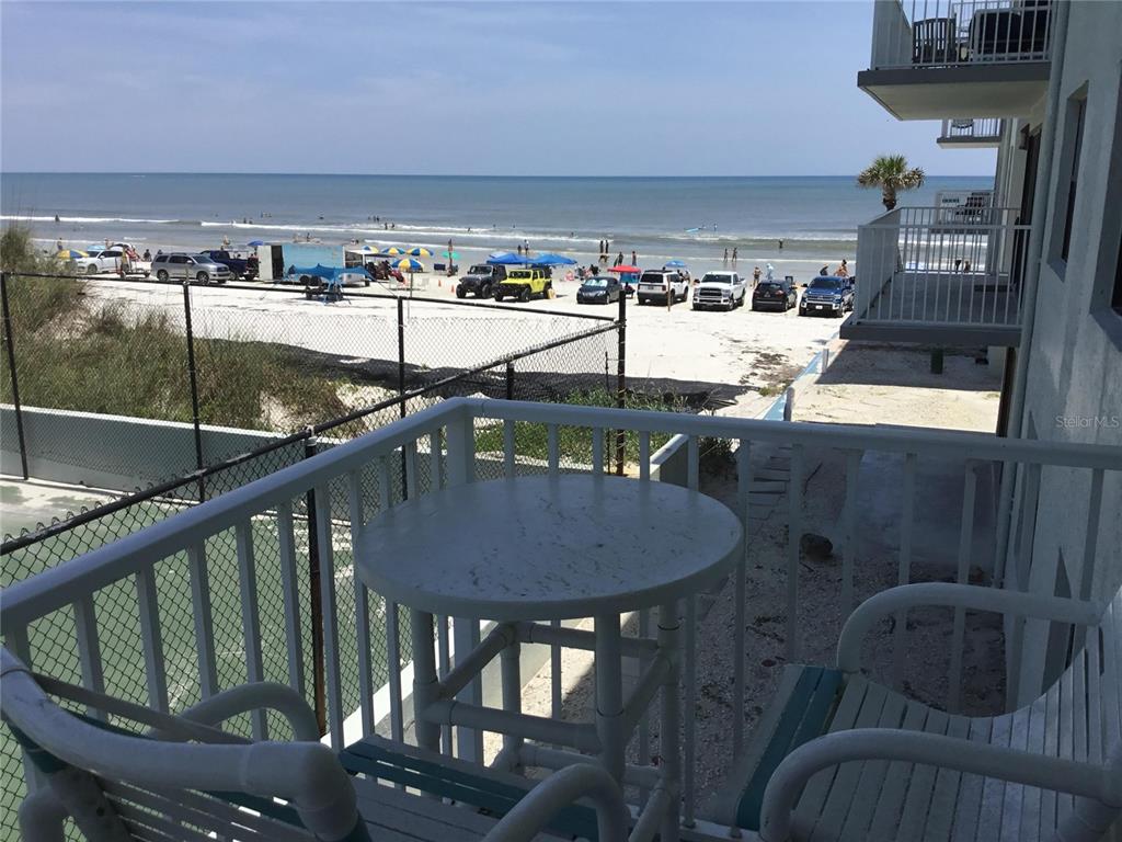 A balcony with a round table and chairs overlooks a beach with parked vehicles — 1571 S ATLANTIC AVENUE UNIT 212, NEW SMYRNA BEACH, FL