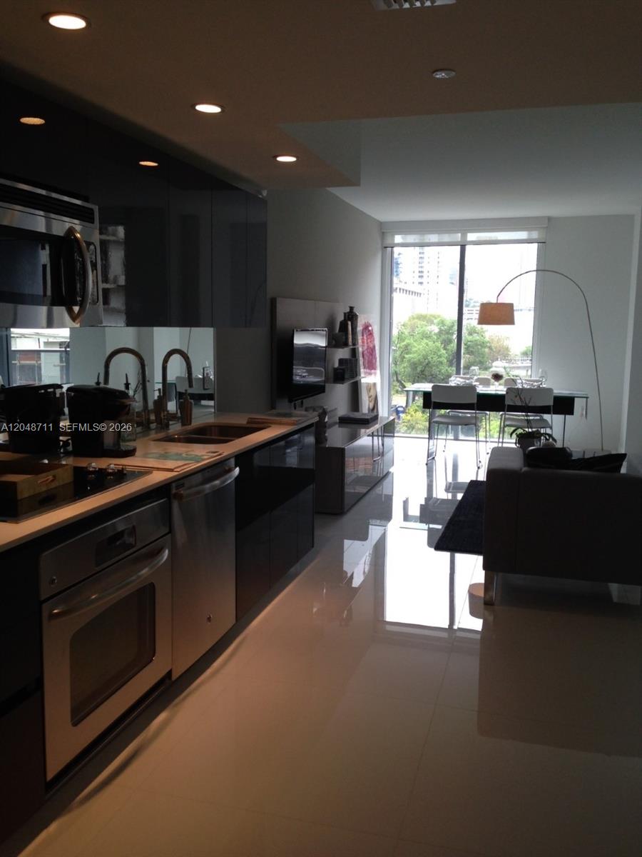 A modern kitchen with dark cabinetry and white tile floors opens into a living area — 31 SE 6 STREET # 603, Miami FL 33131, MIAMI, FL