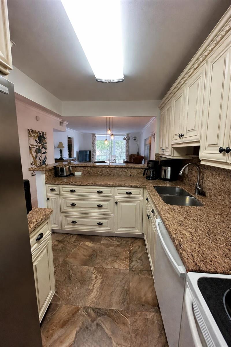 A kitchen with cream cabinets, granite countertops, and brown tile flooring overlooks a living area — 400 SE 10th Street # 202, Deerfield Beach FL 33441, DEERFIELD BEACH, FL