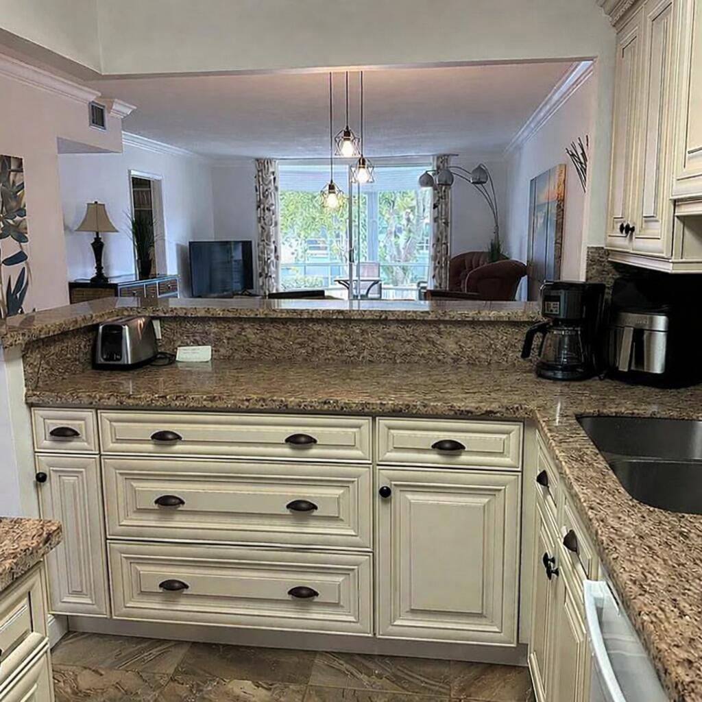A kitchen with granite countertops and off-white cabinets overlooks a living area with balcony views — 400 SE 10th Street # 202, Deerfield Beach FL 33441, DEERFIELD BEACH, FL