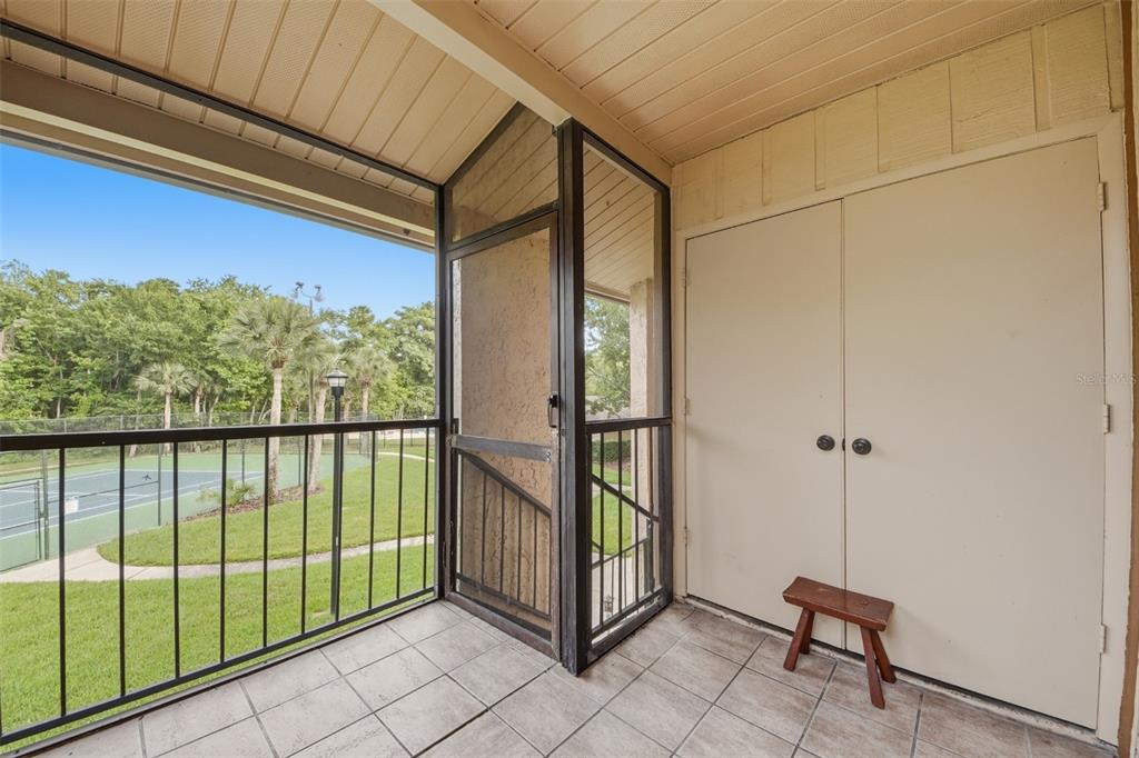 A tiled balcony features a screened enclosure, a storage closet, and a view of tennis courts — 4800 S SEMORAN BOULEVARD UNIT 107, ORLANDO, FL