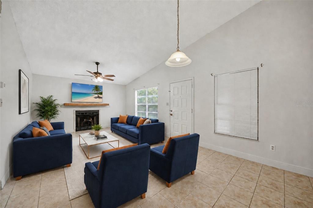 A living room features a fireplace, blue sofas, tile flooring, and a vaulted ceiling — 4800 S SEMORAN BOULEVARD UNIT 107, ORLANDO, FL