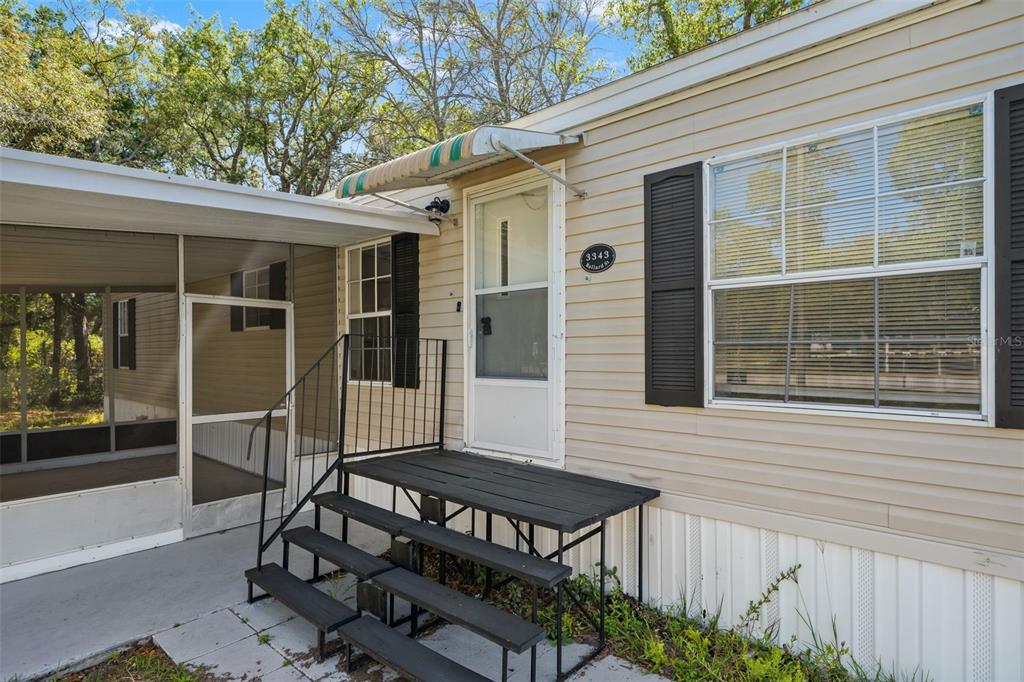 A mobile home exterior features beige siding, a screened porch, and black metal front steps — 3345 BALLARD STREET, SPRING HILL, FL