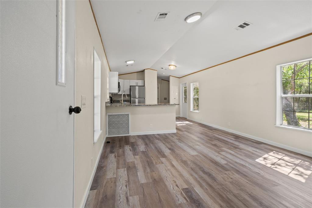 An open-concept living area features wood-look flooring, beige walls, and a kitchen with a breakfast bar — 3345 BALLARD STREET, SPRING HILL, FL