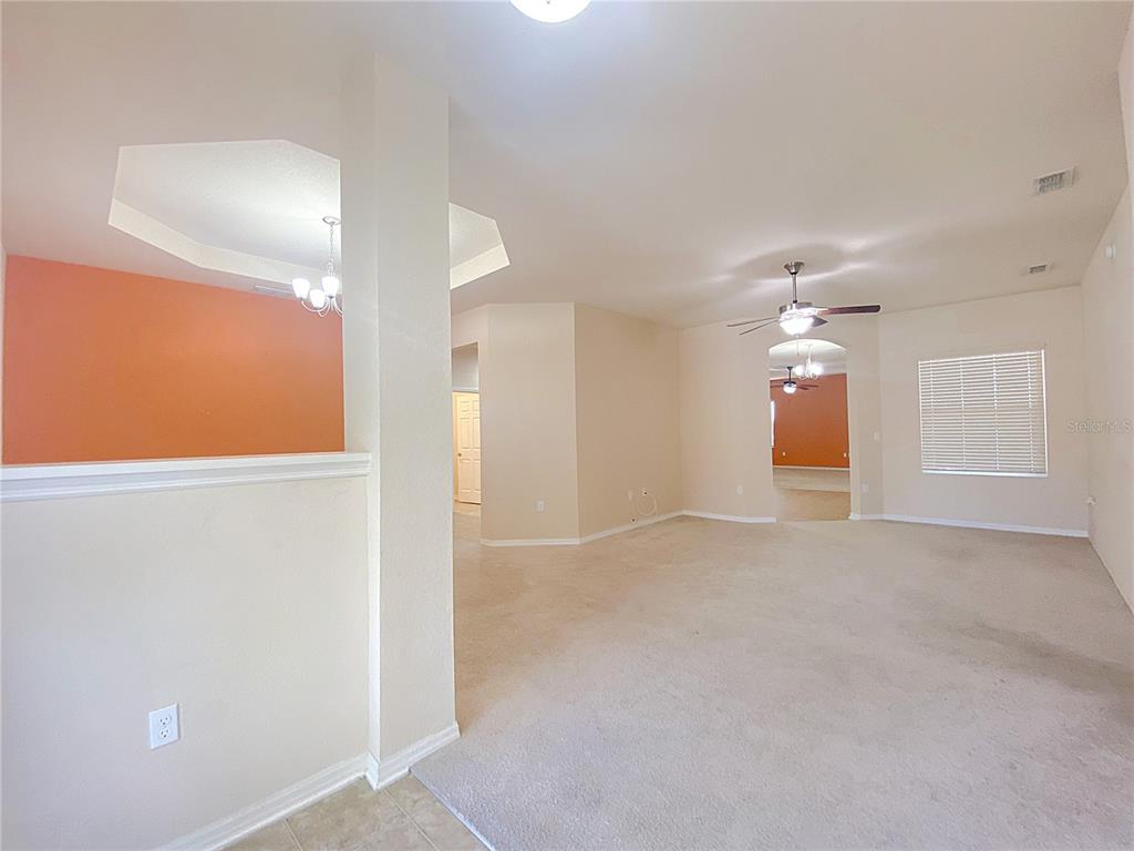 A spacious living area features beige carpeting, neutral walls, and an orange accent wall — 4311 MANDOLIN BOULEVARD, WINTER HAVEN, FL