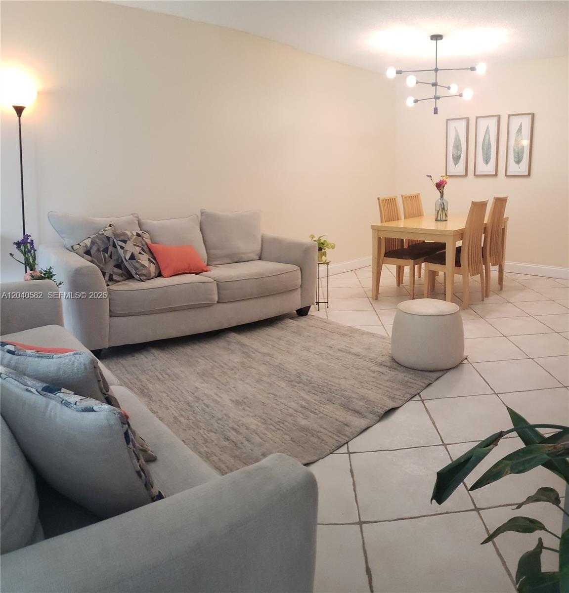 A living and dining area features light-colored sofas, a rug, and a modern chandelier — 550 Oaks Ln # 202, Pompano Beach FL 33069, POMPANO BEACH, FL