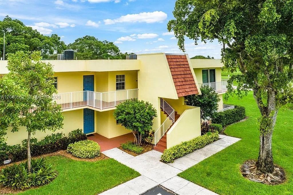 A two-story yellow apartment building features a red-tiled roof section and exterior staircases — 550 Oaks Ln # 202, Pompano Beach FL 33069, POMPANO BEACH, FL