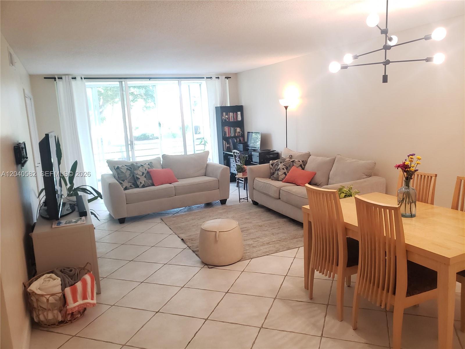 A living and dining area features tile floors, two sofas, and a modern light fixture — 550 Oaks Ln # 202, Pompano Beach FL 33069, POMPANO BEACH, FL