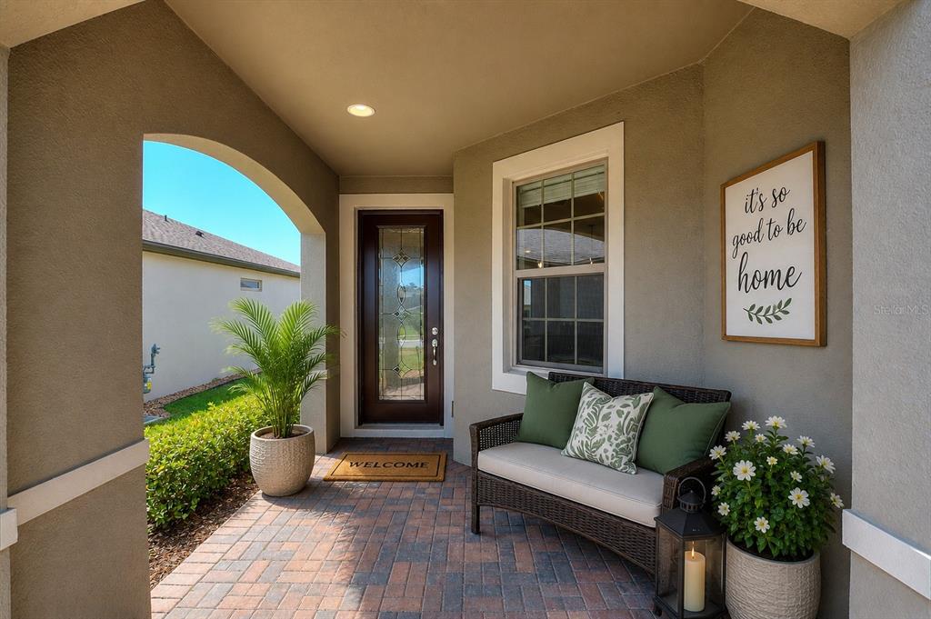 A covered front porch features a wicker bench, a potted plant, and a welcome mat — 406 TORTOSA COURT, DAVENPORT, FL