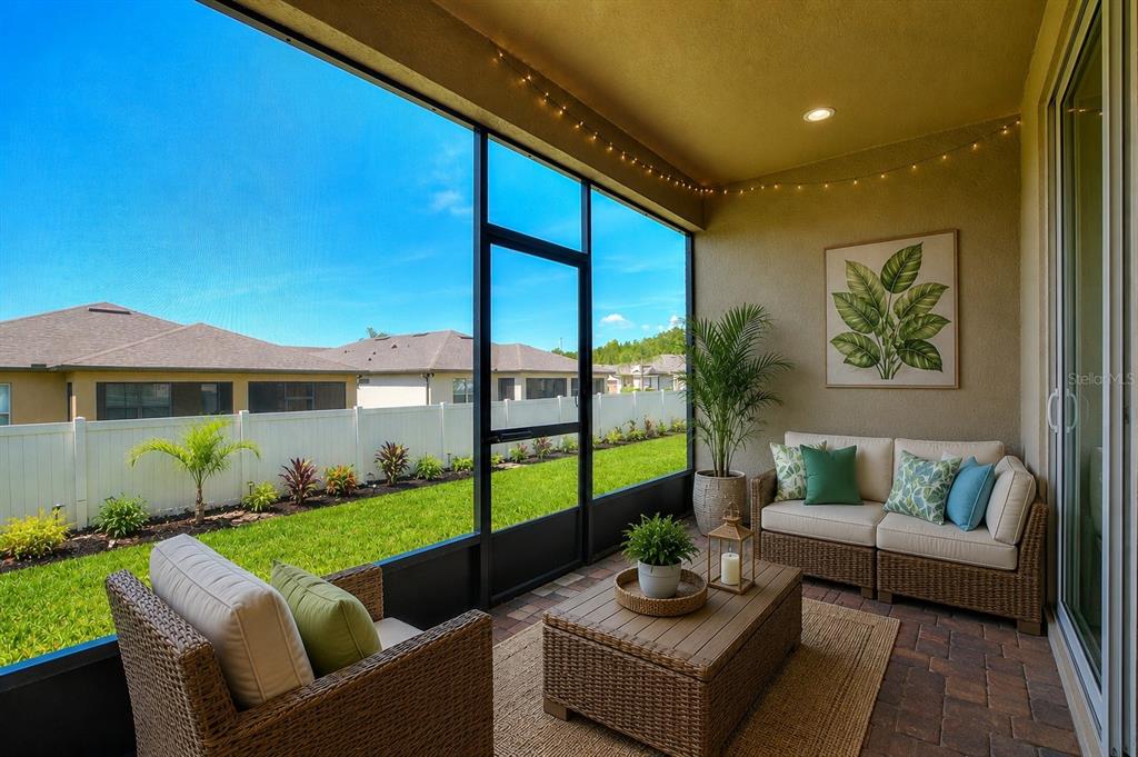 A screened-in patio features wicker furniture, a coffee table, and a view of a backyard — 406 TORTOSA COURT, DAVENPORT, FL