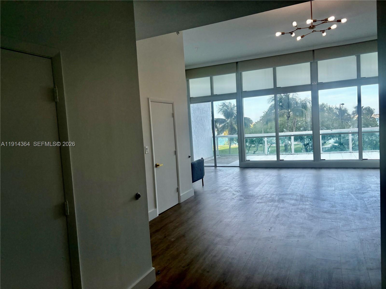 An empty room with wood-look flooring, white walls, and floor-to-ceiling windows overlooking a balcony — 1800 N Bayshore Dr # 306, Miami FL 33132, MIAMI, FL