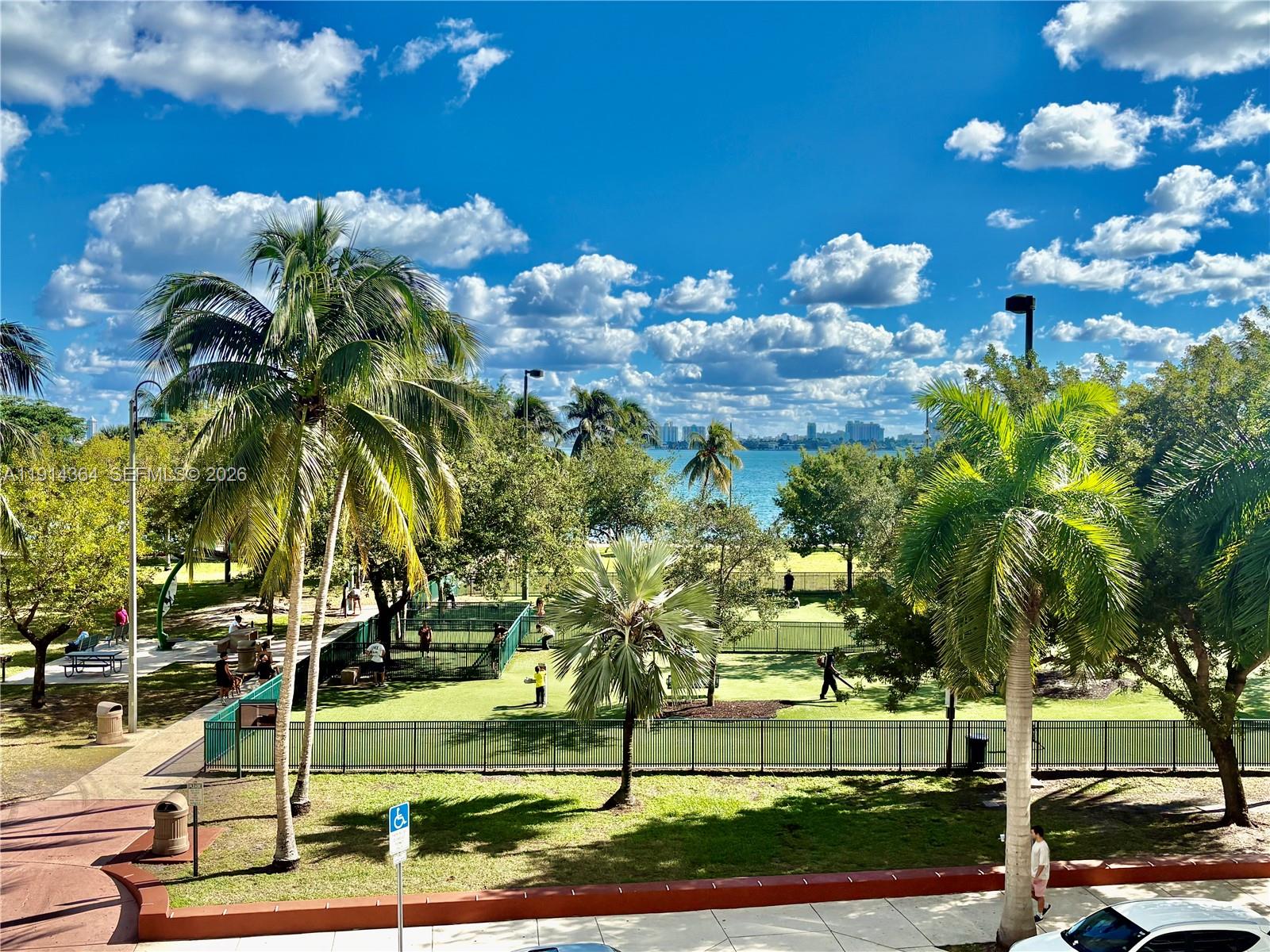 A view of a fenced park with palm trees and a body of water beyond — 1800 N Bayshore Dr # 306, Miami FL 33132, MIAMI, FL