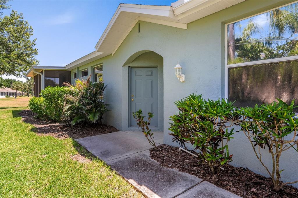 A light blue house exterior features a gray front door, a concrete walkway, and landscaping — 1204 HUNTINGTON GREENS DRIVE UNIT 1204, SUN CITY CENTER, FL