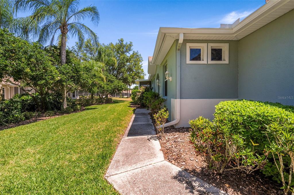 A concrete walkway runs along the side of a house with light blue exterior walls — 1204 HUNTINGTON GREENS DRIVE UNIT 1204, SUN CITY CENTER, FL